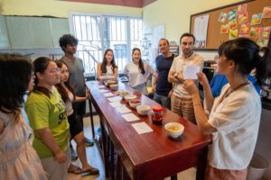 A group stands around a long table set with small bowls for a tasting