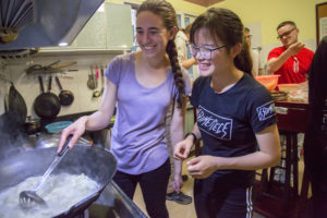 Two people smile while cooking dumplings in a wok in a kitchen