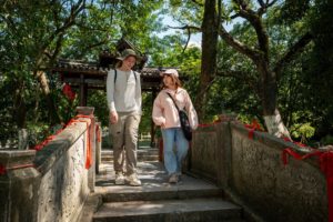 Two people walk down old stone steps under shady trees
