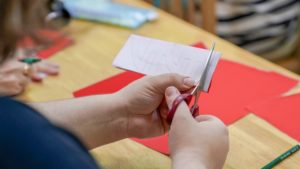Hands cut folded red paper with scissors at a table