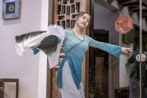 A dancer in a flowing blue dress performs with wide arm movements