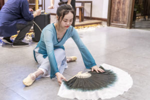 A dancer kneels with a large fan during a floor performance