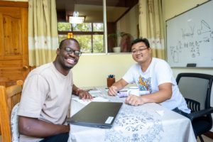 A student and teacher laugh together at a table with a laptop