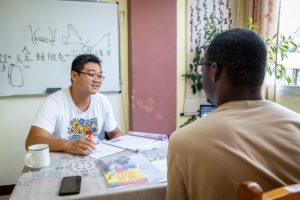 A teacher talks with a student at a table below a whiteboard with drawings