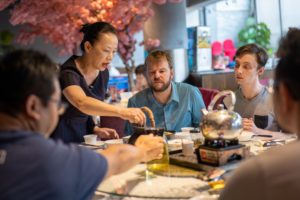 A woman pours tea for a group seated around a restaurant table
