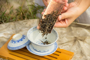 Hands tip loose tea leaves into a blue and white teacup