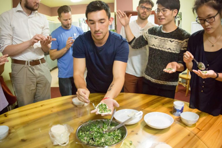 Students and teachers folding dumplings around a table at CLI