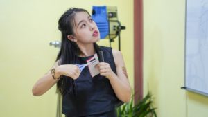 A paper-cutting instructor holds up scissors and folded white paper while explaining