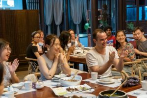 People laugh and clap around a dinner table full of dishes