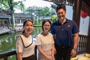 Three people pose on a balcony above a garden pond