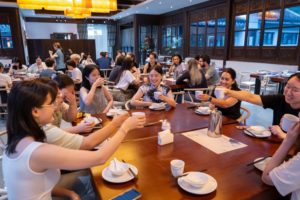 Diners sit around long tables full of dishes in a restaurant hall