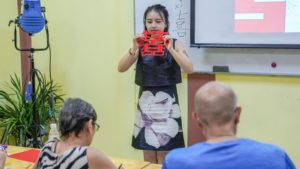 An instructor holds up a finished red paper-cut design for the class