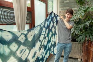 A person holds up a large blue tie-dye cloth by a window