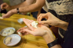 Hands fold a dumpling wrapper over filling
