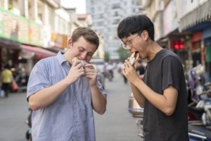 Two friends eat buns together on a city street