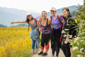 Four friends pose on a path beside golden rice terraces