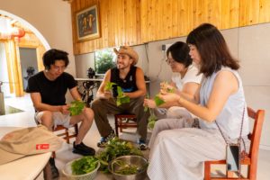 People sit together picking and preparing fresh greens in a wooden room
