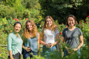 Four women pose together in a sunlit flower garden