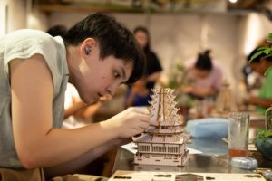 A man with earbuds fits pieces onto a wooden pagoda model