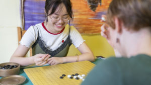 A woman smiles while placing stones on a Go board during a game