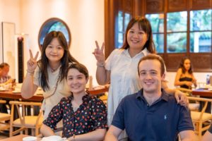 Four people pose with peace signs at a restaurant table