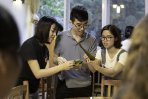Three people learn to wrap zongzi around a table