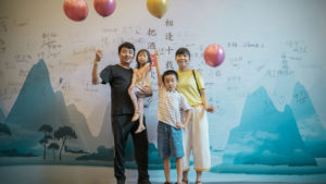 A small group poses in front of a blue mountain mural with balloons