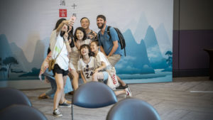 A group crowds together for a selfie in front of a mountain mural