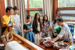 Students watch a tie-dye demonstration around bowls of dye