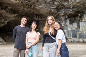 Four friends pose in front of a cave wall