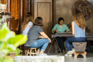 A small group in a wooden room watches a guzheng lesson