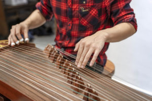 Hands pluck the strings of a guzheng