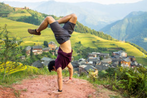 A person does a handstand on a hillside above rice terraces