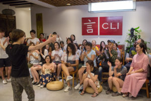 A seated audience watches a performer in a room with a CLI sign