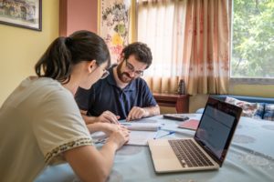 A student and teacher study together at a table with a laptop