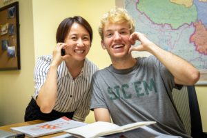 A teacher and student smile and pose at a desk with textbooks