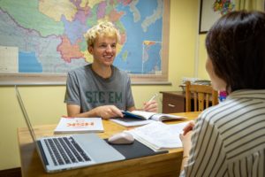 A smiling student sits at a laptop in front of a large wall map