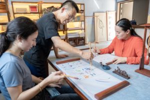 A teacher guides students painting with brushes at a long table