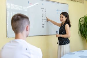 A teacher points to pinyin on a whiteboard while a student watches