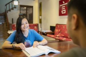 A student smiles while studying with a textbook at a lobby table