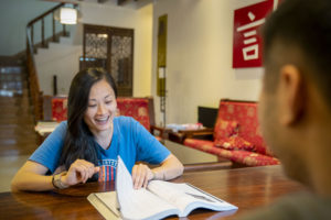 A smiling student reads a textbook at a table in the CLI Center lounge