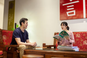 A student and teacher with a textbook talk across a table in the lobby
