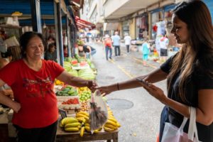 A woman pays a smiling vendor for fruit at a street market