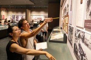 A man and a woman point at old photos on a museum wall