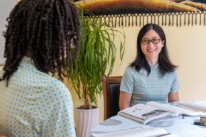 A smiling teacher in a qipao sits across the table from a student