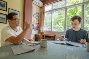 A teacher explains a point to a student at a table with textbooks