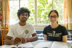 A student and teacher smile at a table with textbooks by a window