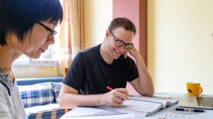 A student writes in a textbook while a teacher watches