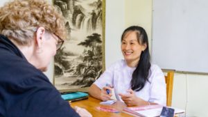 A teacher smiles at a student in front of a mountain scroll painting