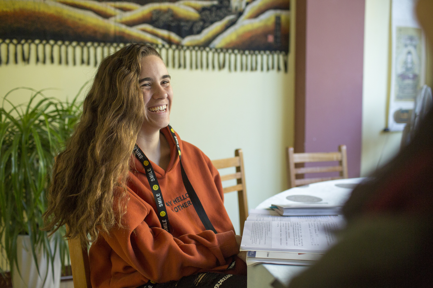 Person in an orange sweater sits indoors and looks off to the side.